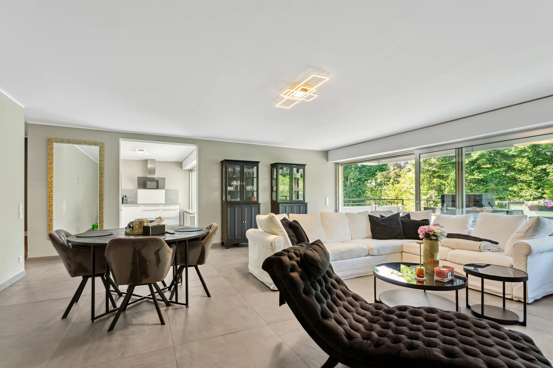 Modernes, helles Wohnzimmer mit offener Küche, großen Fenstern, gemütlicher Sitzecke und Blick ins Grüne“