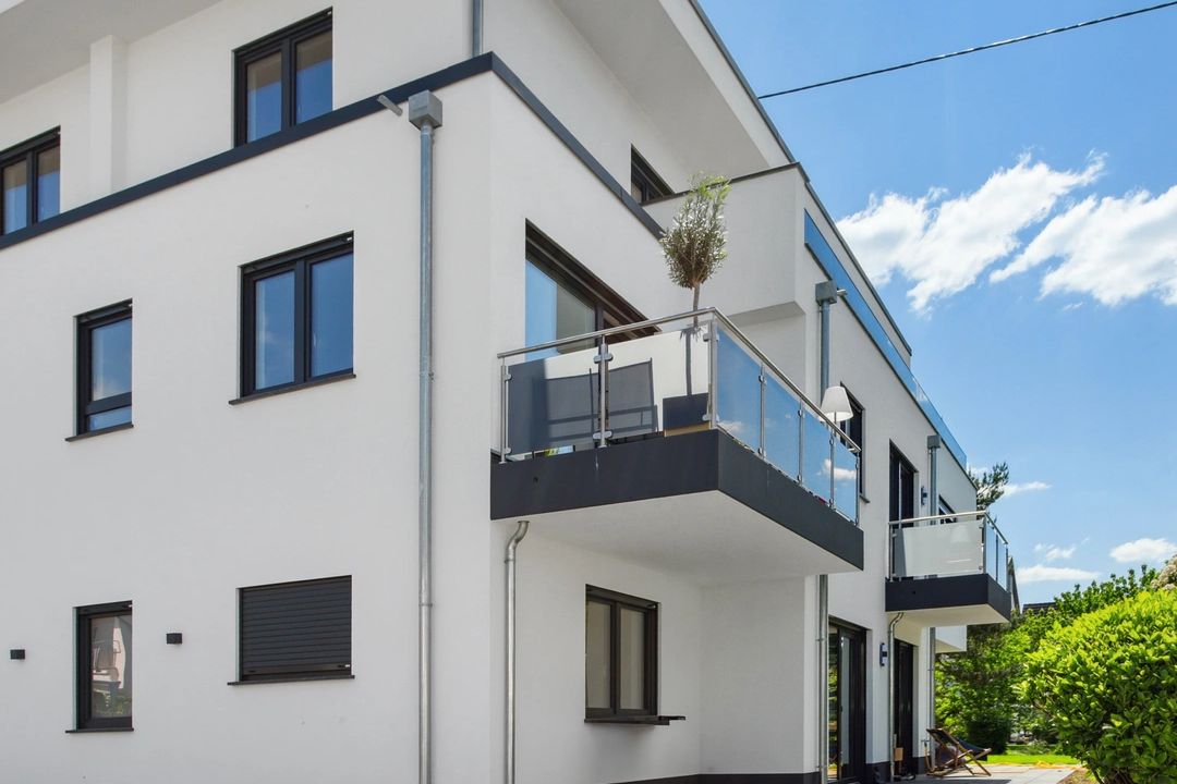 Weißes Mehrfamilienhaus mit moderner Architektur, großem Balkon und gepflasterter Einfahrt.