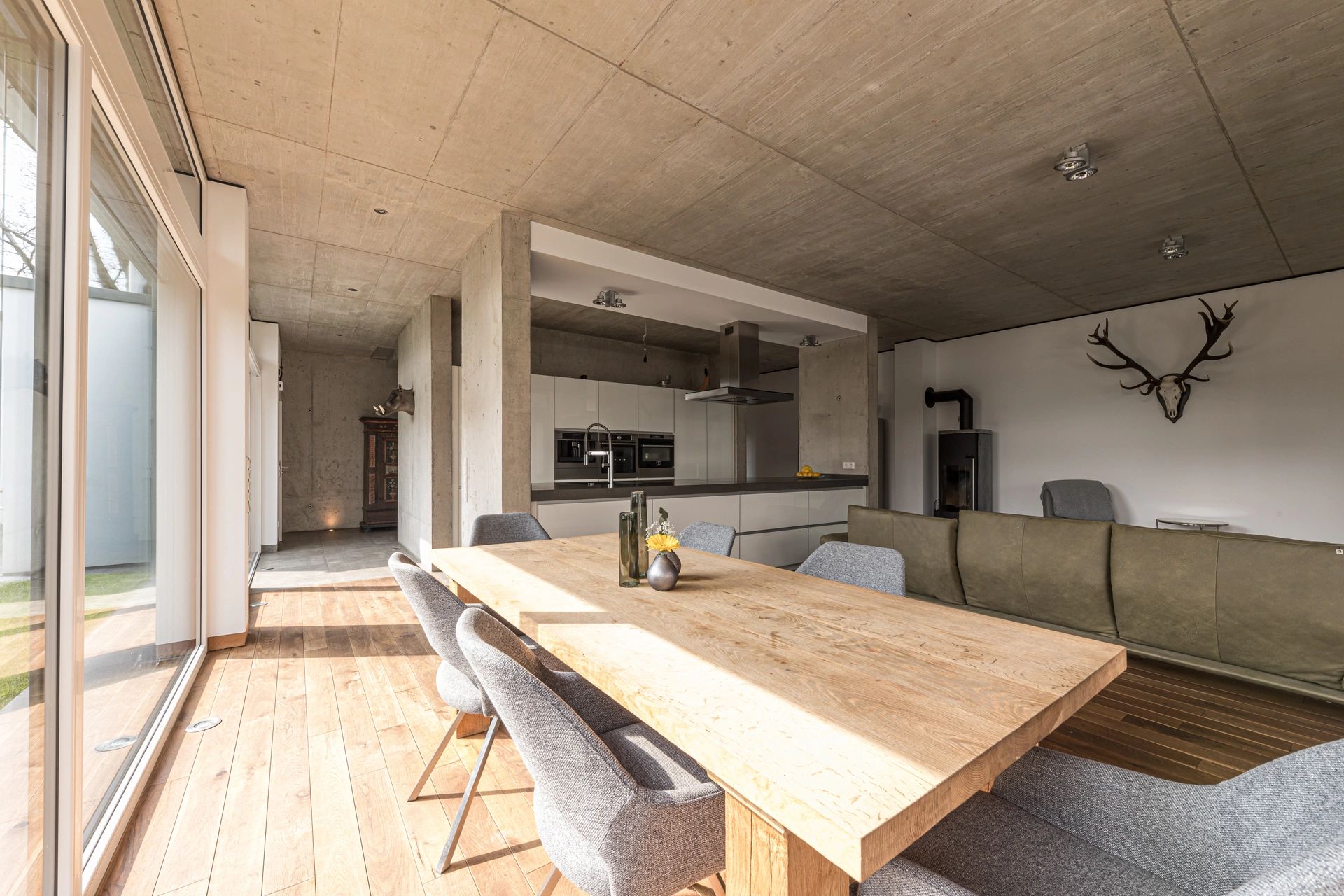 Offener Wohn- und Essbereich mit moderner Küche, Sichtbetondecke und Holzfußboden – D+P Immobilienmakler Siegburg unterstützt bei der Suche nach designorientierten Immobilien.